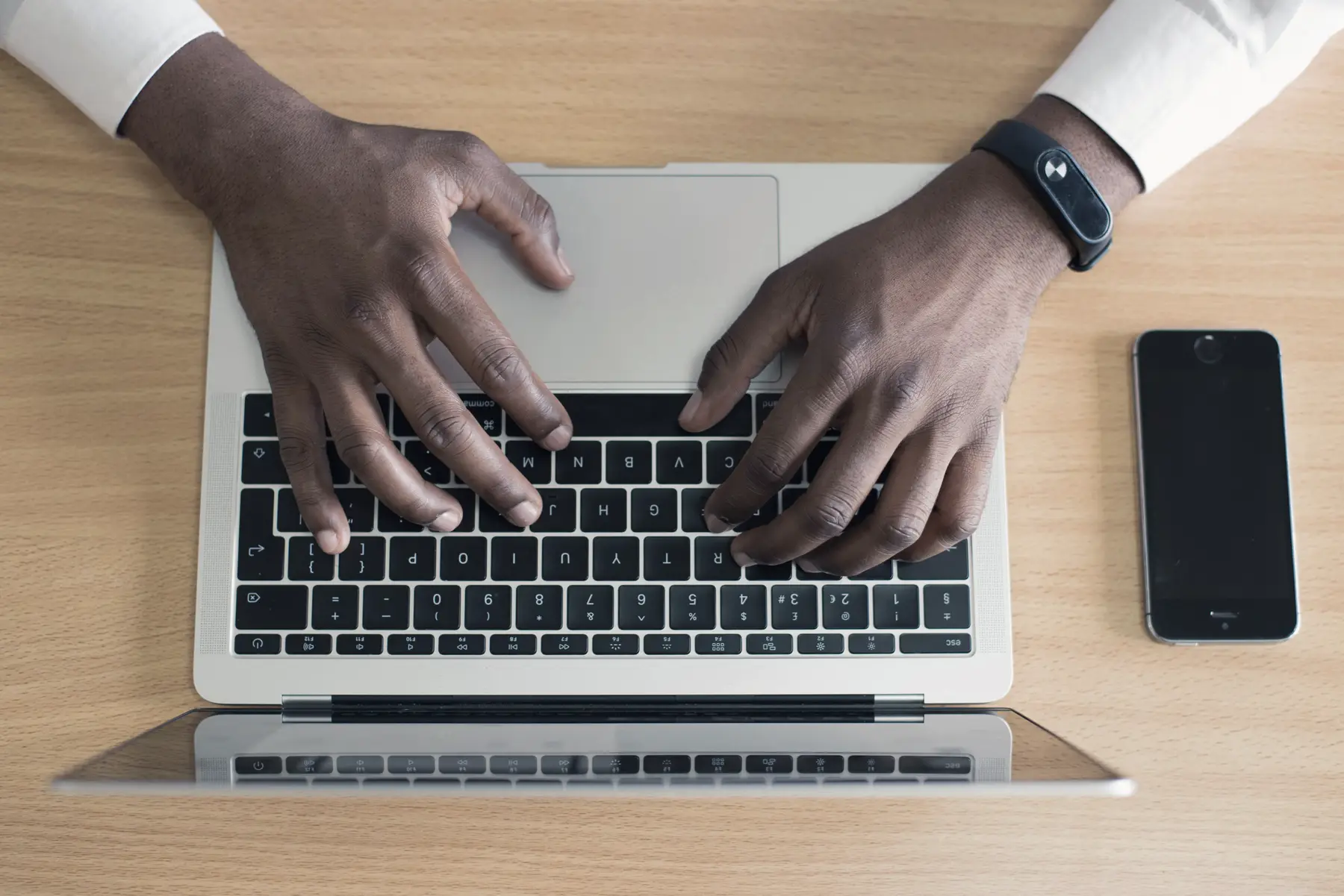Close view of hands working at a laptop beside a notebook