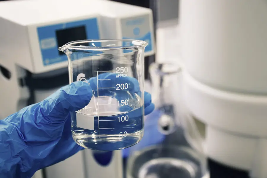 A gloved hand holding a laboratory beaker beside analytical equipment